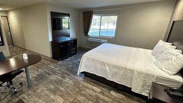 A hotel room with a bed, a desk, a TV, a window with curtains, and a heater.