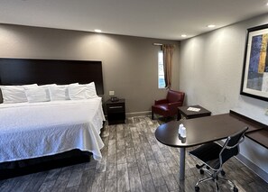 A hotel room with a bed, a desk, a chair, a nightstand, and a window with curtains. - Red Roof Inn Hayward (Hayward)