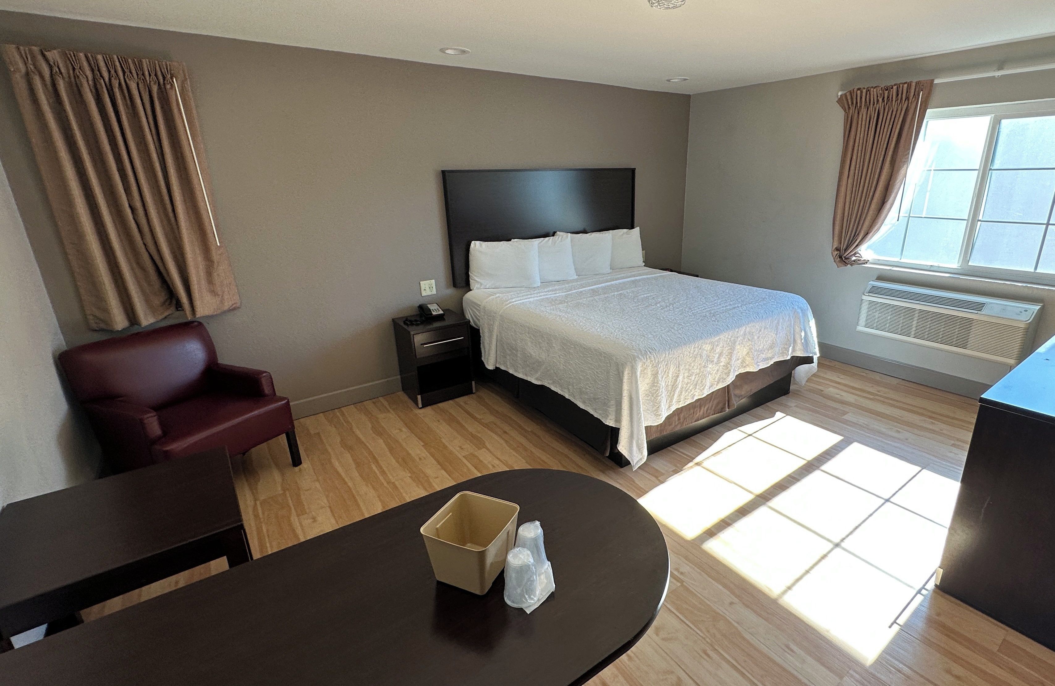A hotel room with a bed, a desk, a chair, a nightstand, and a window with curtains.