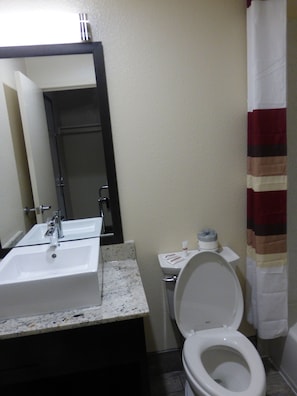 A bathroom with a sink, mirror, toilet, and shower curtain. - Red Roof Inn Hayward (Hayward)