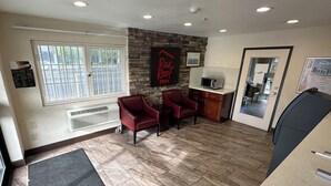 A reception area with a stone wall, two red chairs, a microwave, and a door leading to a room. - Red Roof Inn Hayward (Hayward)