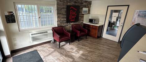 A reception area with a stone wall, two red chairs, a microwave, and a door leading to a room.