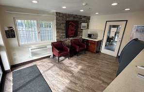 A reception area with a stone wall, two red chairs, a microwave, and a door leading to a room. - Red Roof Inn Hayward (Hayward)