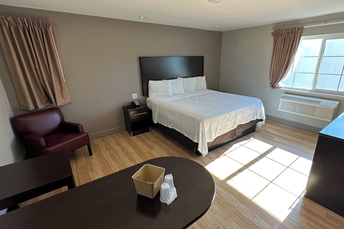 A hotel room with a bed, a desk, a chair, a nightstand, and a window with curtains.