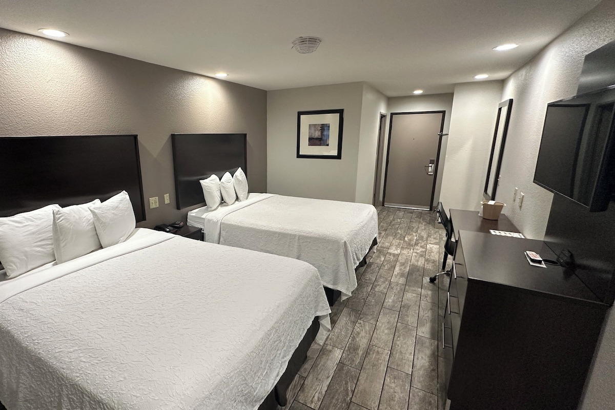 A hotel room with two beds, a desk, a TV, and a door leading to another room.