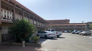 Un parcheggio con diverse auto, un edificio con balconi e una palma.