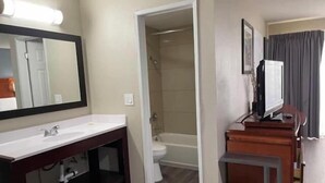 Un bagno d'hotel con lavandino, specchio, doccia, servizi igienici e una televisione su un mobile in legno.