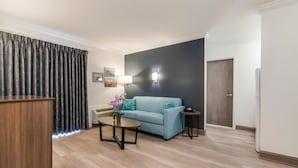 Un salon moderne avec un canapé bleu clair, une table basse et une lampe. On aperçoit, au fond, une armoire en bois et une porte.