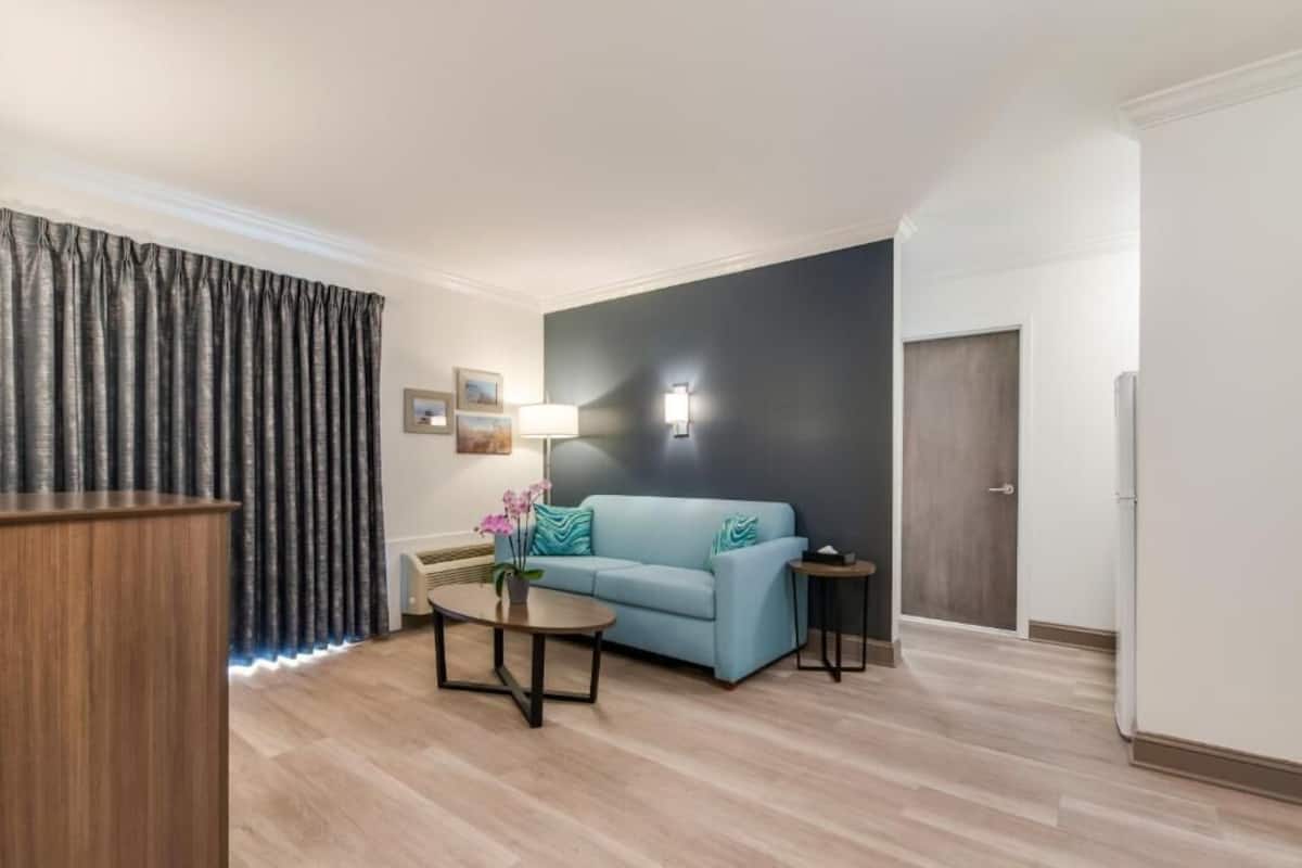 Un salon moderne avec un canapé bleu clair, une table basse et une lampe. On aperçoit, au fond, une armoire en bois et une porte.