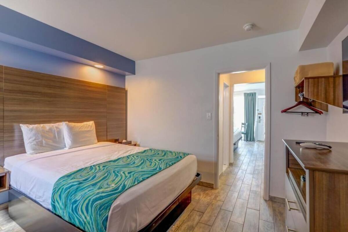 Une chambre d’hôtel moderne dotée d’un grand lit, d’une tête de lit en bois, d’un petit bureau et d’un coin cuisine.