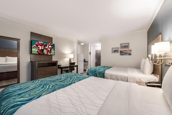 A hotel room with two beds, a desk, a TV, and a lamp.