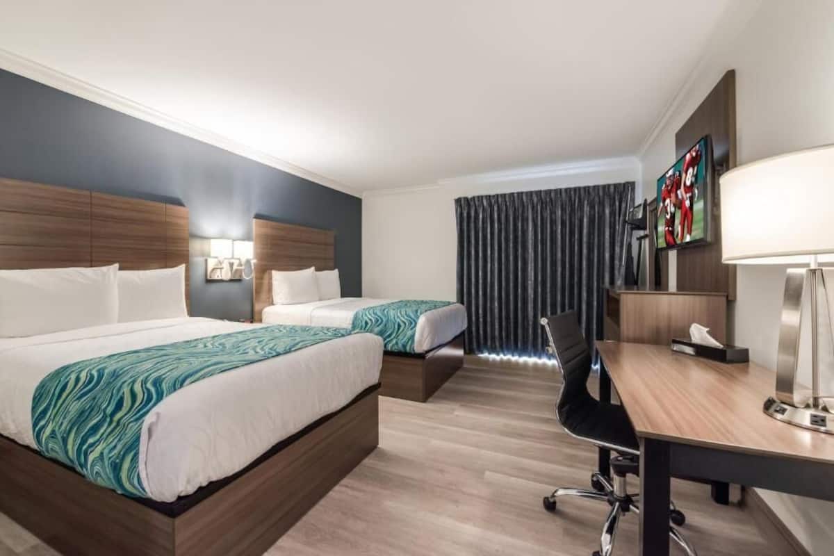 Une chambre d’hôtel avec deux lits, un bureau, une chaise, une télévision et une fenêtre avec des rideaux.
