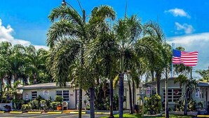 A building with a flag, surrounded by palm trees. - Richard s Motel Extended Stay (Hallandale Beach)
