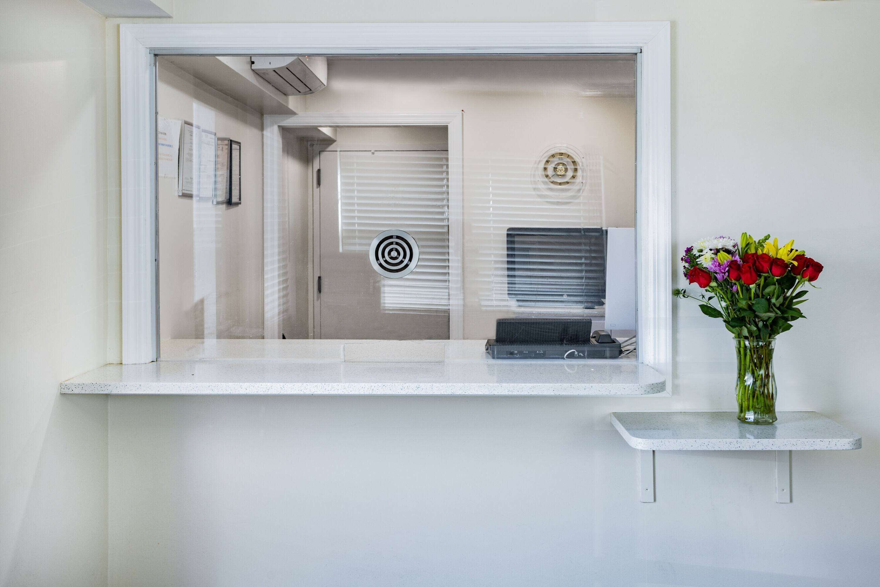 A reception area with a counter, a vase with flowers, and a door with blinds.