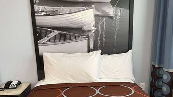 Habitación de hotel con cama, mesita de noche con teléfono y pared con una fotografía grande de barcos.