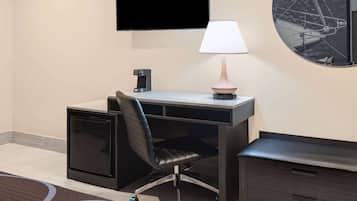 A hotel room with a desk, chair, TV, lamp, and a small cabinet.