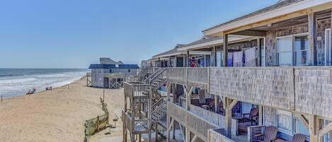 A beachfront hotel with multiple balconies, wooden deck, and ocean views.