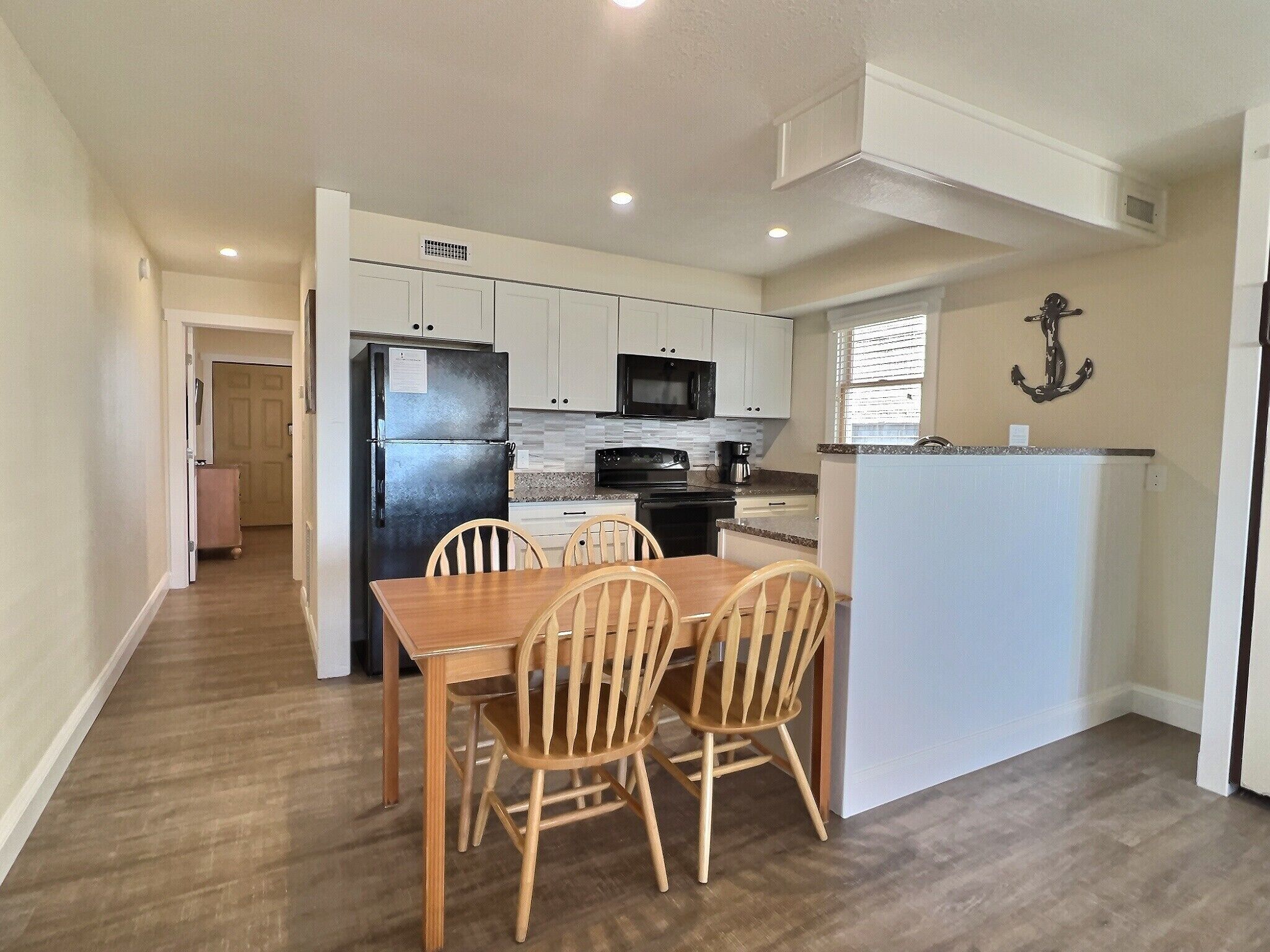 A modern kitchen with white cabinets, a black refrigerator, and a wooden dining table with four chairs.