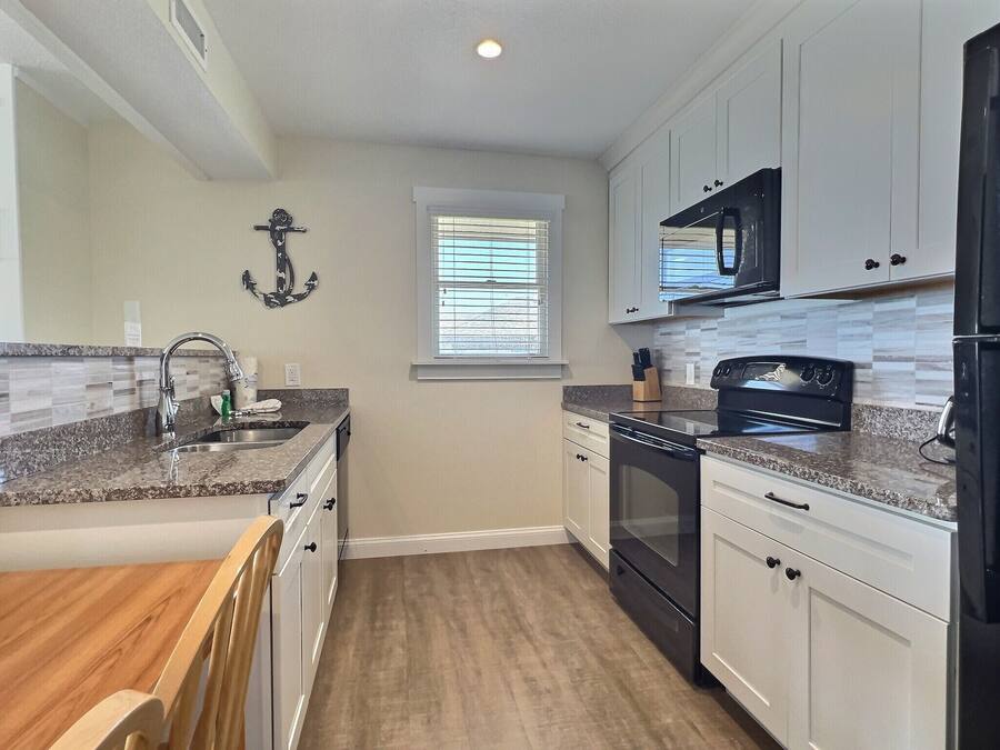 A kitchen with white cabinets, a black microwave, and a stainless steel sink.