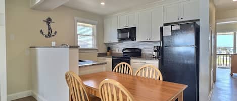 A modern kitchen with white cabinets, a black refrigerator, and a dining area with wooden chairs and a table.