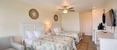 A hotel room with two beds, a ceiling fan, a desk with a TV, and a small seating area.