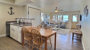A spacious living area with a dining table and chairs, a kitchen with a sink and cabinets, and a view of the ocean through large windows. - Lighthouse View Oceanfront Lodging (Buxton)