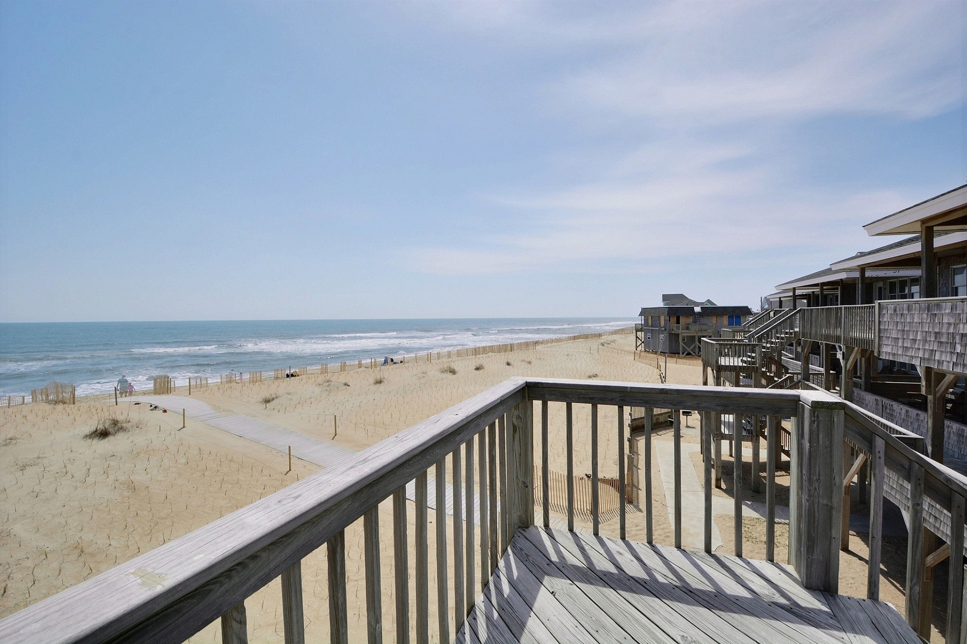 A beach view from a wooden deck with a sandy beach and ocean in the background.