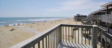 A beach view from a wooden deck with a sandy beach and ocean in the background.