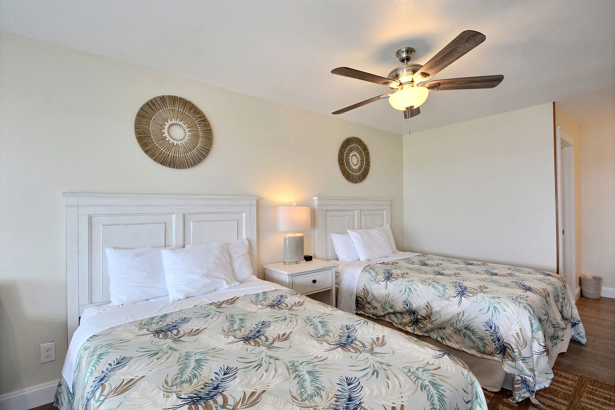 A hotel room with two beds, a ceiling fan, and decorative wall art.