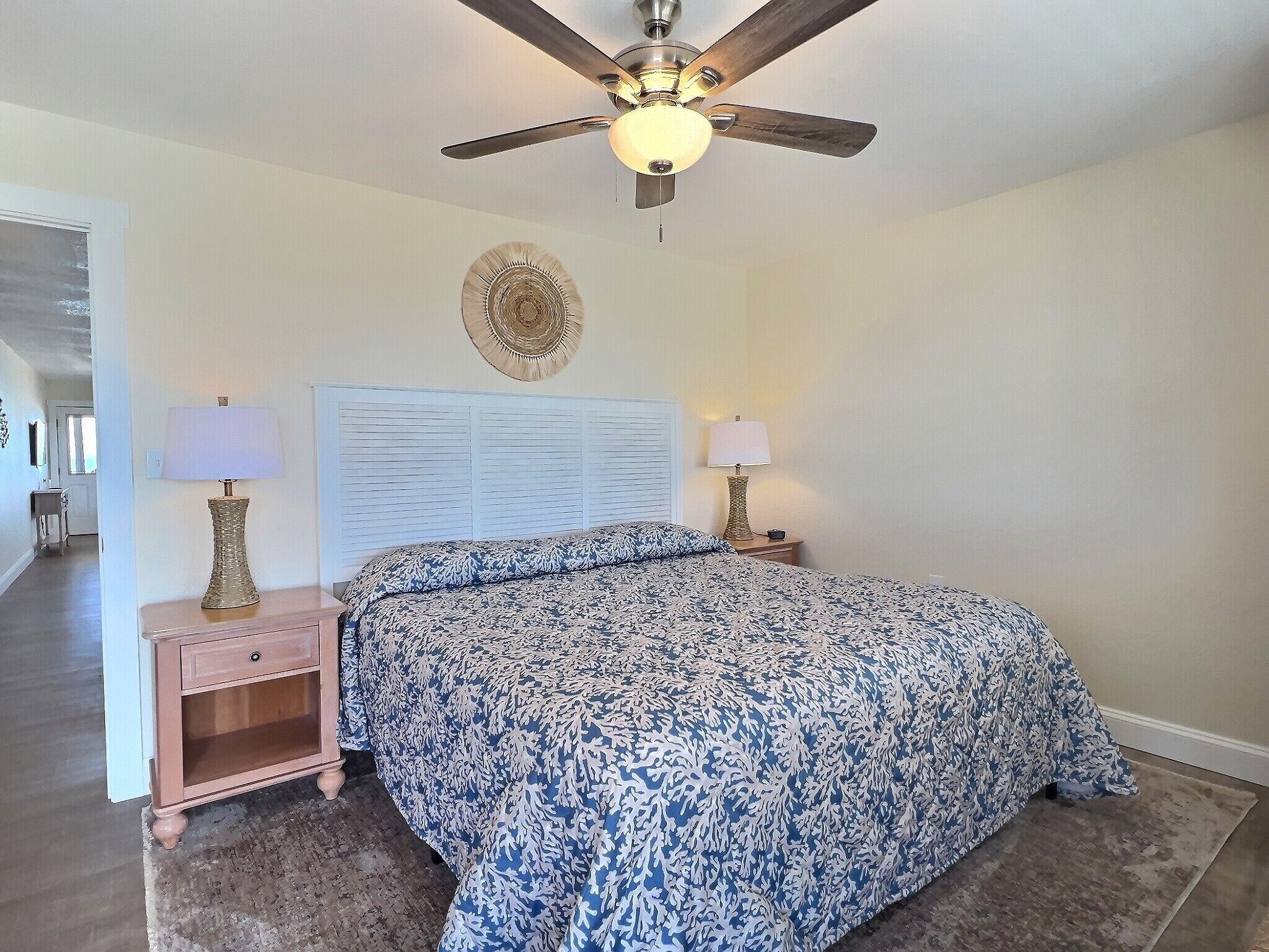 A bedroom with a bed, two bedside lamps, a ceiling fan, and a decorative wall piece.