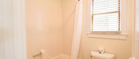 A bathroom with a bathtub, toilet, and a window with blinds.