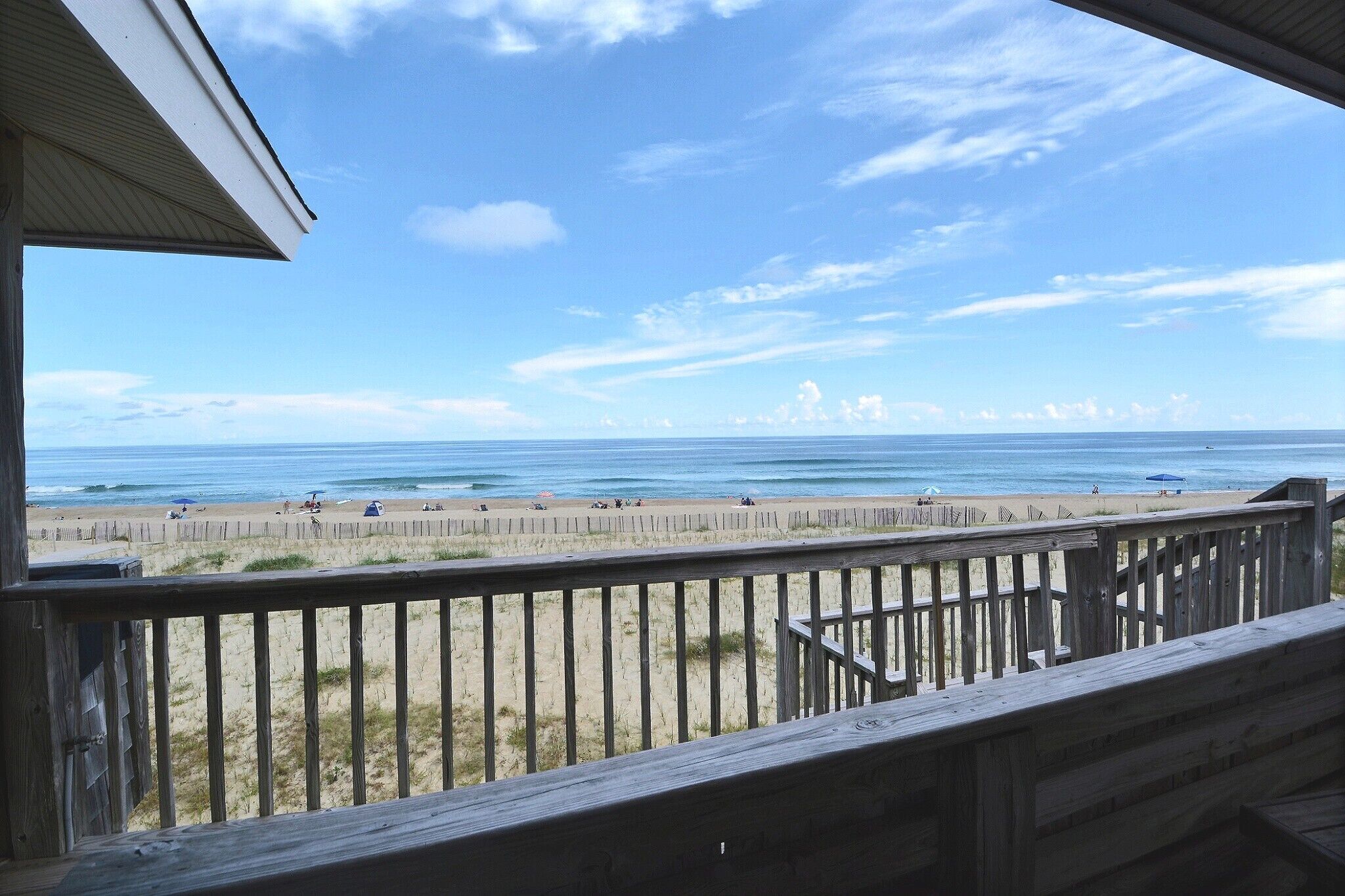 A beach view from a wooden deck with a railing, sandy beach, and ocean.