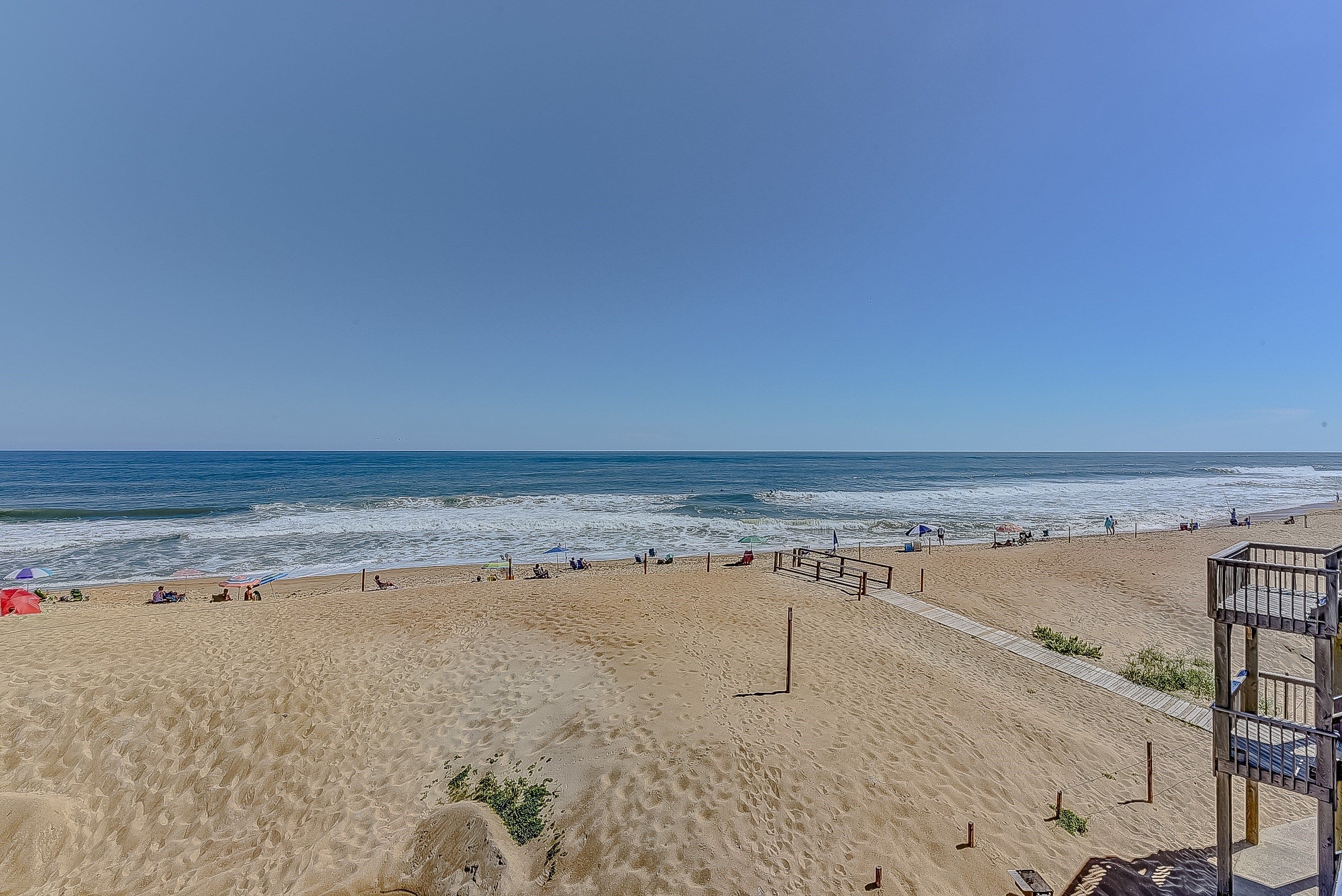 A beach with a wooden walkway and a lifeguard tower.