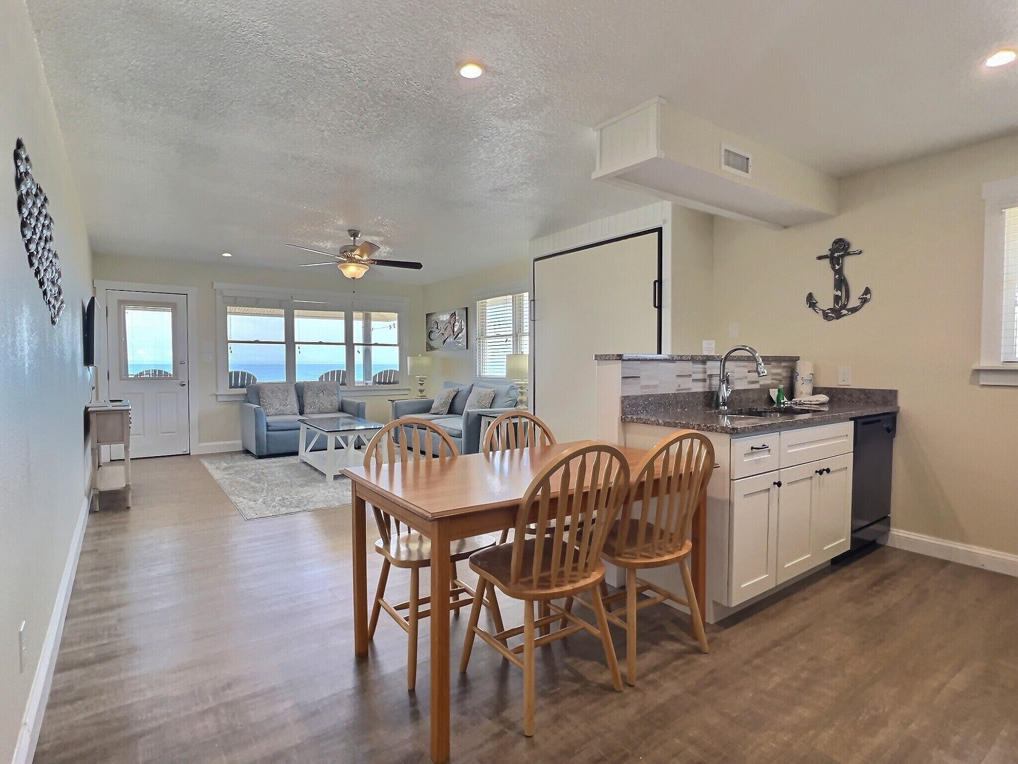 A spacious living area with a dining table and chairs, a kitchen with a sink and cabinets, and a ceiling fan.