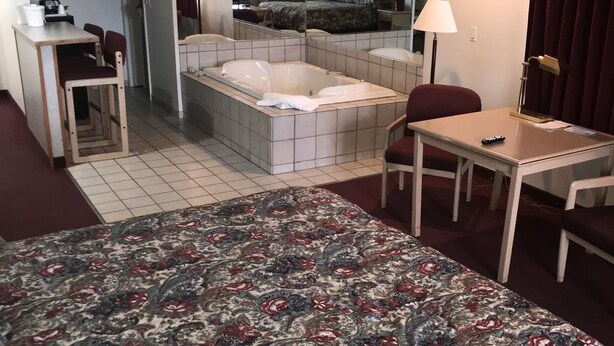 A hotel room with a large bed, a small desk, a chair, a sofa, a bathtub, and a mirror. - Thunderbird Motel (Missoula)