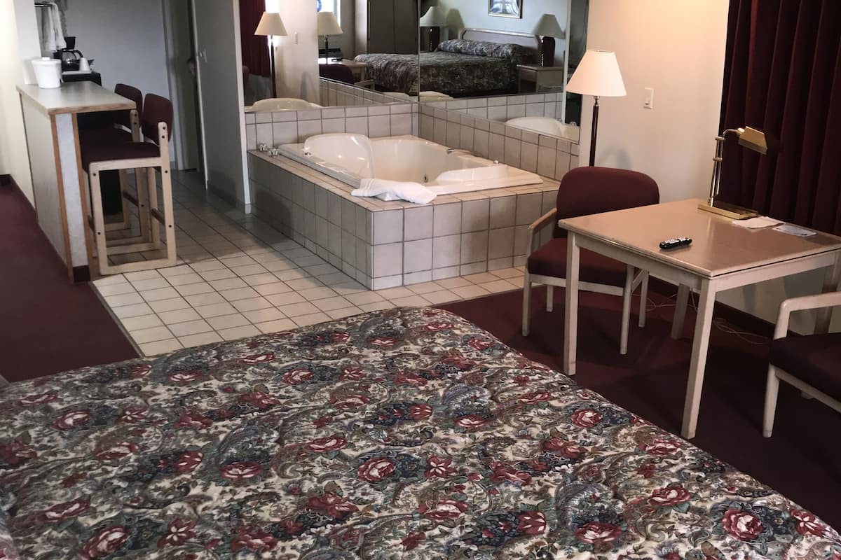 A hotel room with a large bed, a small desk, a chair, a sofa, a bathtub, and a mirror.