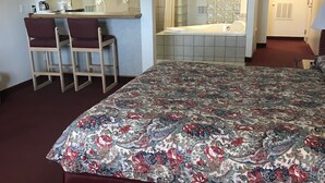 A hotel room with a large bed, a sitting area with a desk and chairs, a bathroom with a bathtub, and a shower. - Thunderbird Motel (Missoula)