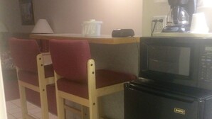 A compact kitchen with a microwave, a refrigerator, and a coffee maker. There are two wooden chairs with red cushions. - Thunderbird Motel (Missoula)