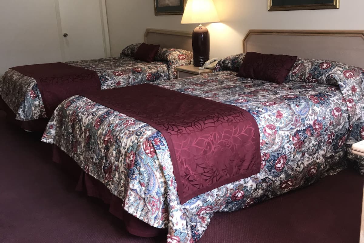 A hotel room with two beds, a bedside table with a lamp, and a door.