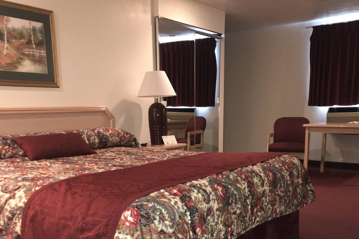 A hotel room with a large bed, a desk, a chair, and a window with curtains.