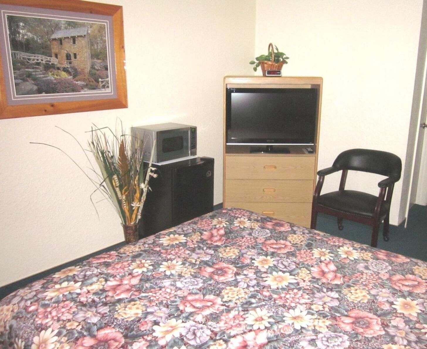 A bedroom with a bed, a television on a cabinet, a chair, and a framed picture on the wall.
