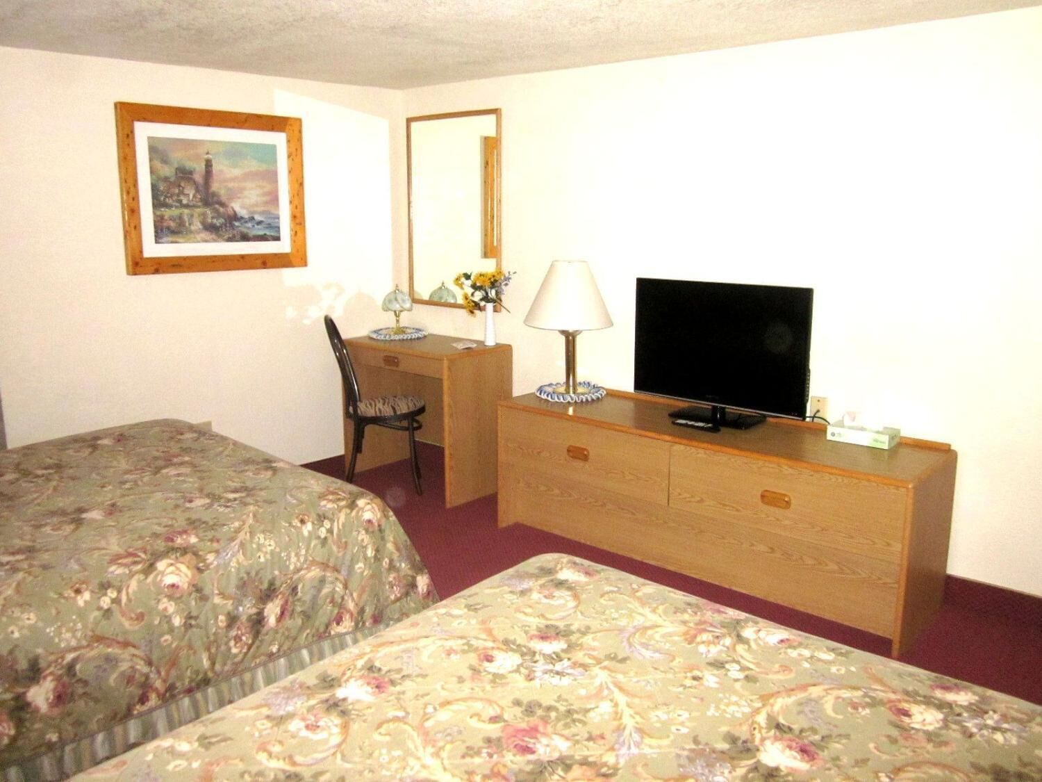A hotel room with two beds, a desk with a chair, a television, and a dresser.