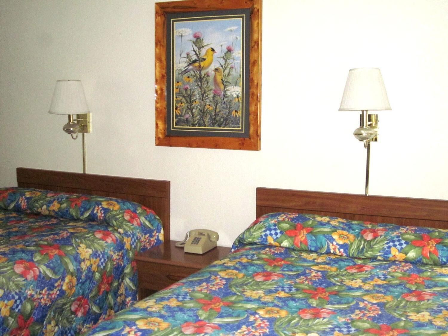 A hotel room with two beds, each with a floral bedspread. There is a framed painting of birds on the wall above the beds.