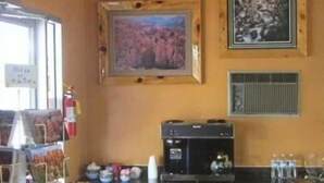 A coffee shop interior with a coffee machine, framed pictures on the wall, and a window with a sign. - Color Country Motel (Panguitch)