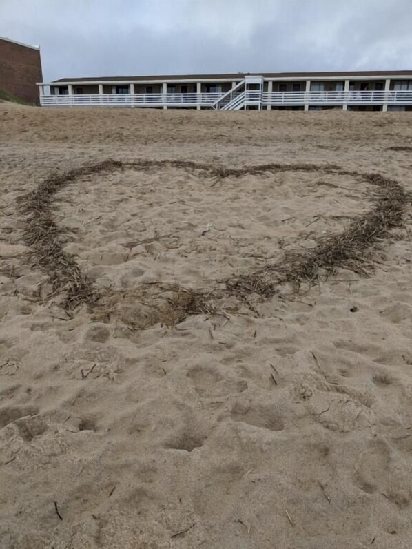 Un dibujo de arena con forma de corazón en una playa, con un edificio al fondo.