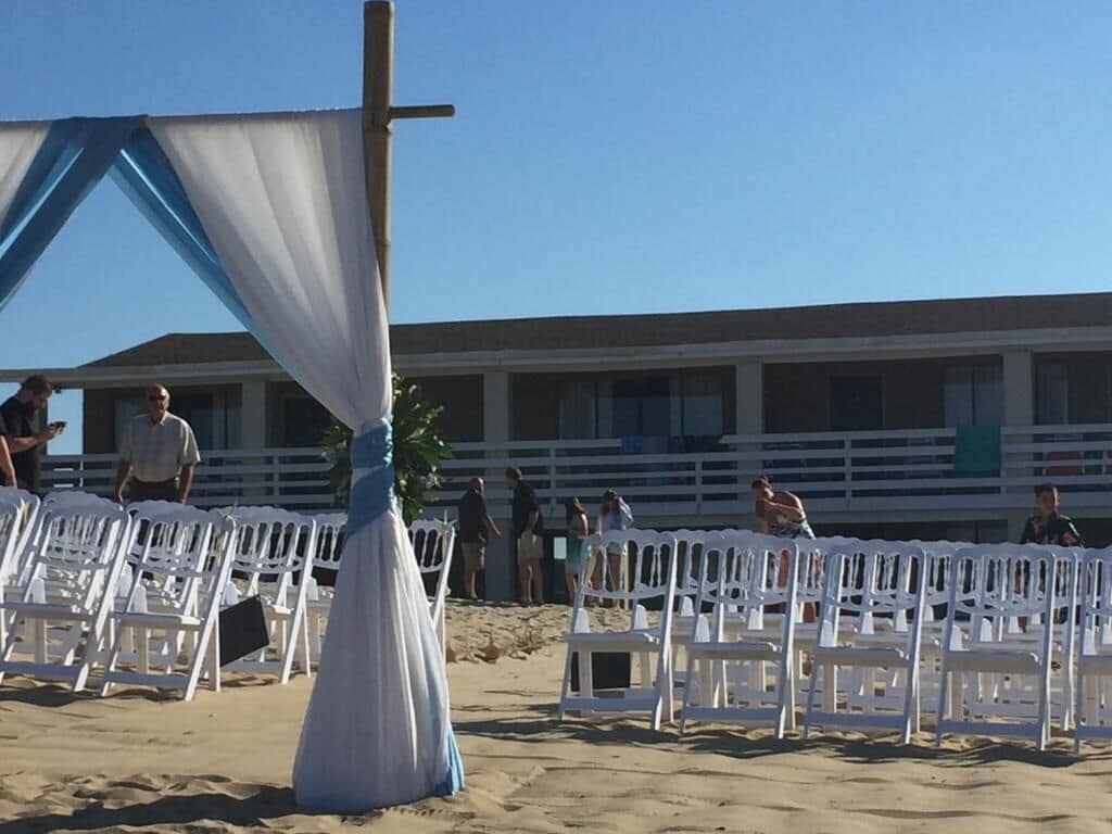 A beachside wedding setup with white chairs and a cross.