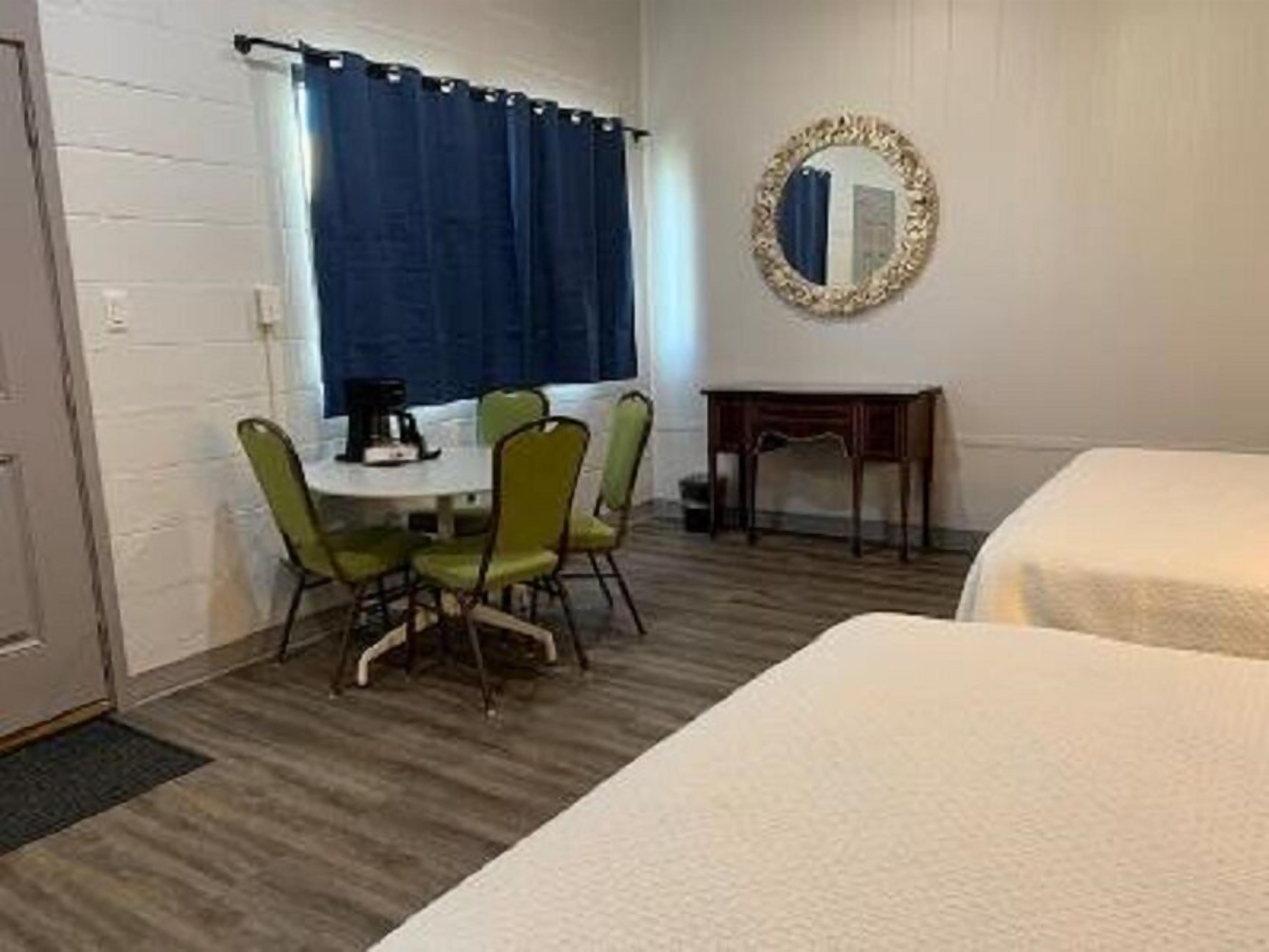 A room with a round dining table, four chairs, a small wooden side table, a bed, and a mirror on the wall.