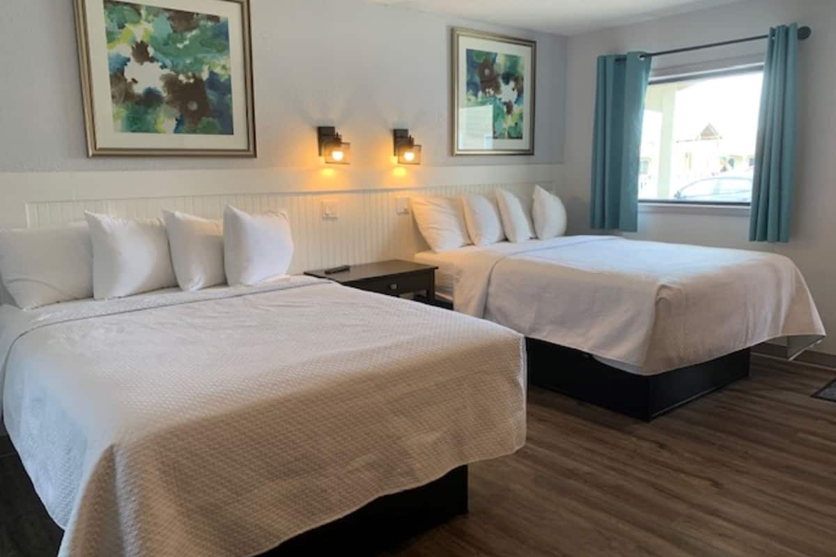 A hotel room with two beds, a nightstand, wall-mounted lights, and artwork on the walls.