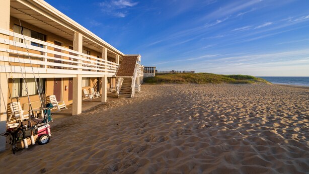 A beachfront hotel with a balcony, beach chairs, and a dune in the background. - Outer Banks Motor Lodge (Kill Devil Hills)