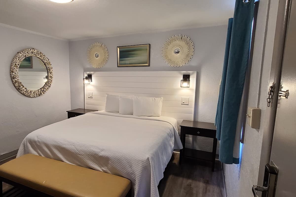 A hotel room with a large bed, a bench, a mirror, and decorative wall art.